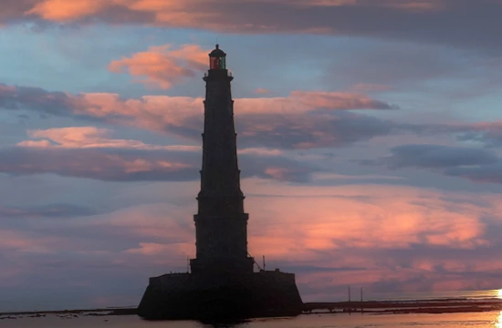 Les activités et loisirs autour de Lacanau. Vue du phare de Cordouan en fin de journée, le phare apparait dans le ciel aux couleurs dégradées de blanc, gris , doré et rosé entre terre et océan