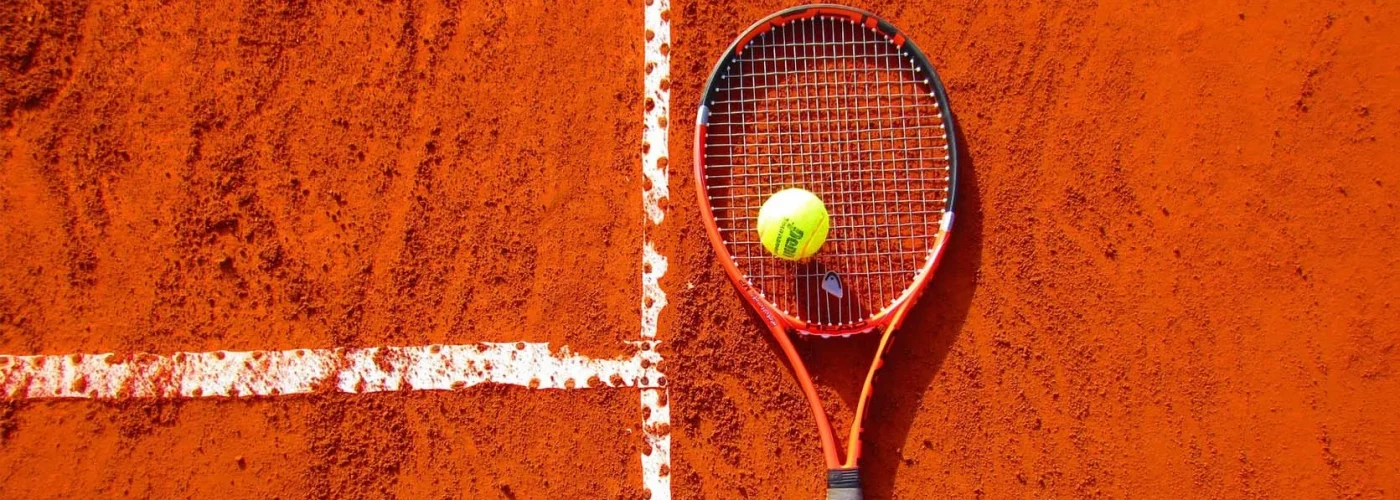Les activités et loisirs autour de Lacanau. Une raquette de tennis et sa balle jaune posée sur de la terre battue