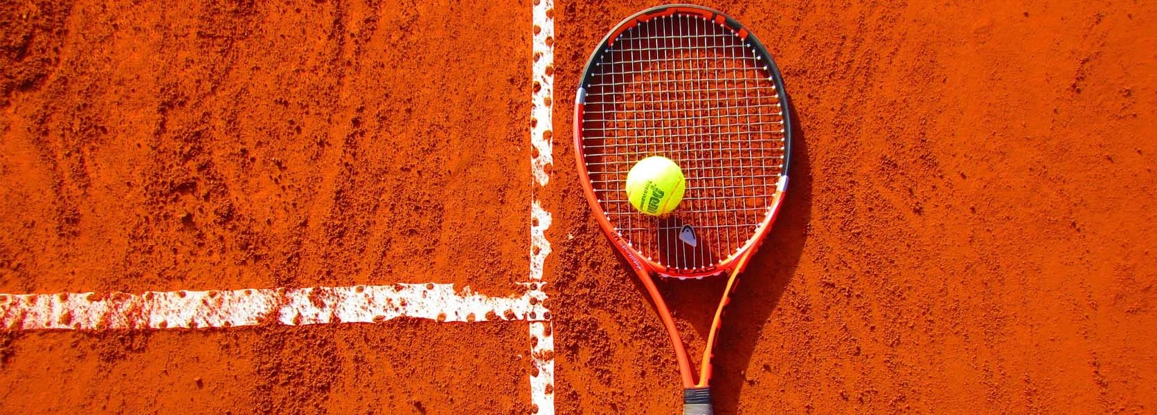 Les activités et loisirs autour de Lacanau. Une raquette de tennis et sa balle jaune posée sur de la terre battue