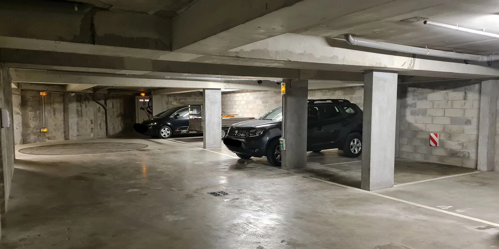 Le parking en sous-sol. Une place disponible par appartement. interdit aux véhicules over size. Au fond, la plateforme qui permet de se placer dans la bonne direction avant de se garer en marche arrière sur la place réservée pour chaque appartement