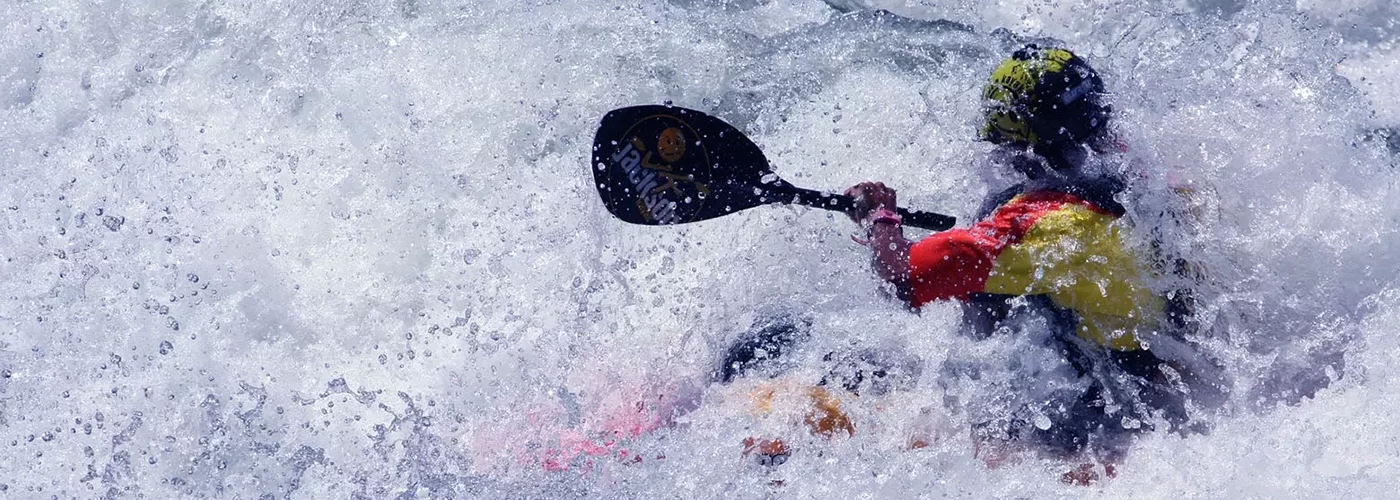 Les activités et loisirs autour de Lacanau. Un kayak dans un bouillon d'écume de la rivière. Le sportif habillé en jaune et rouge pagaie
