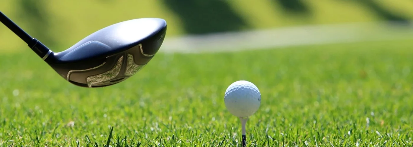 Les activités et loisirs autour de Lacanau. Une balle de golf sur un tee avec l'extrémité d'un driver qui s'apprête à la frapper sur une pelouse verte parfaite