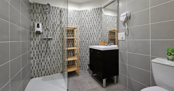 Appart hôtel Pasino n°4 Salle de bain avec toilettes, douche à l'italienne, large vasque surmontée d'un miroir.