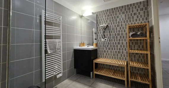 appart hôtel Pasino n°3,salle de bain, son meuble vasque, son miroir, son sèche-cheveux, ses étagères de rangement en bois et son radiateur sèche serviette