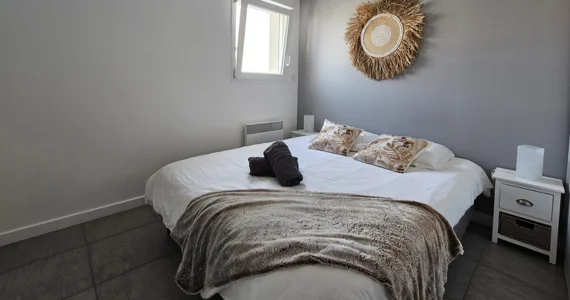 Appart hôtel Pasino n°3 Chambre 2 avec un grand lit en 160/200. 2 oreillers avec des taies décoratives, un plaid et deux serviettes de bain posés au coin du lit