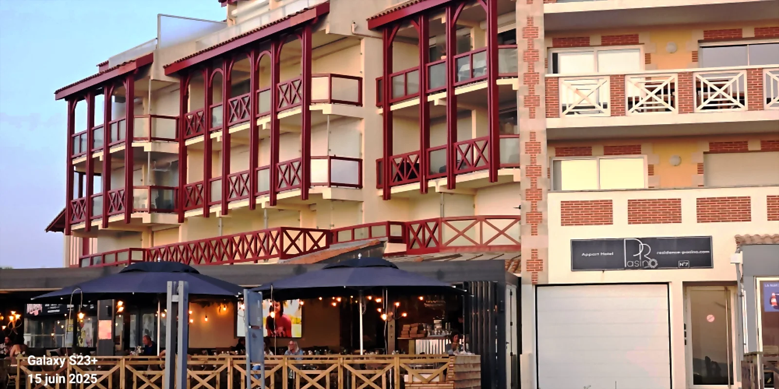 Entrée de la résidence Pasino, on voit l'entrée avec le volet roulant du garage et l'entrée piétonne situés entre 2 terrasses de restaurant . au dessus de l'entrée les terrasses des appartements 1 et 4 Au dessus de l'entrée les appartements de la résidence Pasino