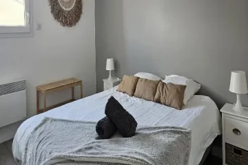 /appart hôtel pasino n°3, chambre N°3 murs blancs et gris, une décoration exotique sur le mur blanc dessous un banc en pin, une suspension au plafond, 2 chevet plus lampes, un lit en 160X200 , 2 oreillers, 3 coussins beiges, un plaid et 2 serviettes sur le lit