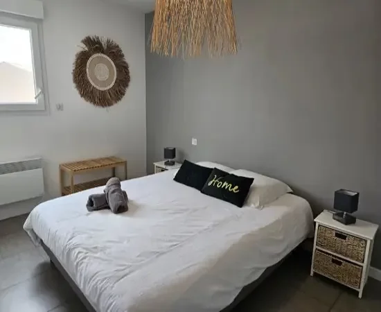 appart hôtel pasino n°6, chambre N°3 murs blancs et gris, une décoration exotique sur le mur blanc dessous un banc en pin, une suspension au plafond, 2 chevets blancs : 2 tiroirs en Osiers plus lampes grises, un lit en 160X200 , 2 oreillers, 2 coussins décoration Vert foncé l'un marqué "Home", 2 serviettes sur le lit