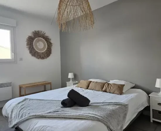 appart hôtel pasino n°3, chambre N°3 murs blancs et gris, une décoration exotique sur le mur blanc dessous un banc en pin, une suspension au plafond, 2 chevet plus lampes, un lit en 160X200 , 2 oreillers, 3 coussins beiges, un plaid et 2 serviettes sur le lit
