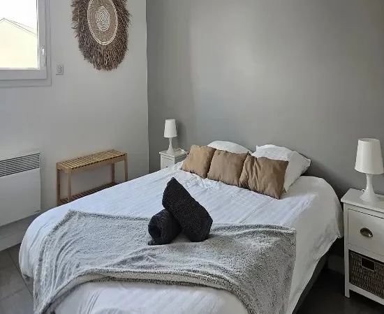 /appart hôtel pasino n°3, chambre N°3 murs blancs et gris, une décoration exotique sur le mur blanc dessous un banc en pin, une suspension au plafond, 2 chevet plus lampes, un lit en 160X200 , 2 oreillers, 3 coussins beiges, un plaid et 2 serviettes sur le lit